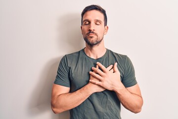 Young handsome man wearing casual t-shirt standing over isolated white background smiling with hands on chest, eyes closed with grateful gesture on face. Health concept.