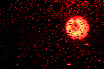 drops of water on the black glass, the glass reflects a round red lamp, use as a background or texture