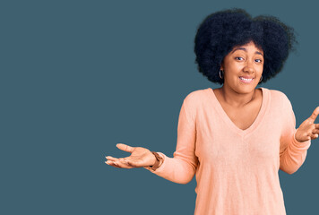 Young african american girl wearing casual clothes clueless and confused expression with arms and...