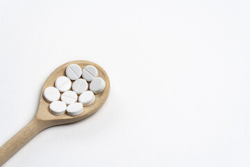 Wooden spoon with round tablets on white background isolated on left below side. Medications on table for coronavirus and pandemic, close up. Free space for text. Pills and drugs. Top view Macro shot