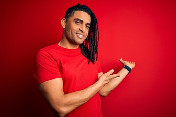 Young handsome african american afro man with dreadlocks wearing red casual t-shirt Inviting to enter smiling natural with open hand