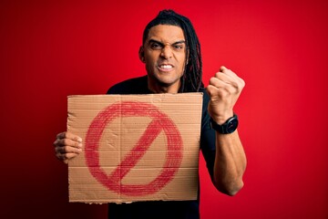 Young handsome african american man with dreadlocks holding banner with prohibited signal annoyed...