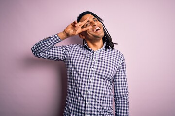 Young handsome african american afro man with dreadlocks wearing casual shirt Doing peace symbol with fingers over face, smiling cheerful showing victory