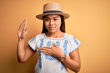 Young beautiful asian girl wearing casual t-shirt and hat standing over yellow background Swearing...