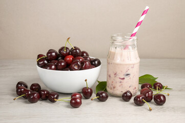 Homemade cherry yogurt smoothie and ripe cherry fruits in a white bowl on a light wooden table.