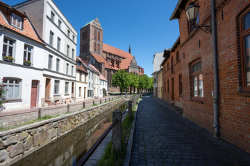 Fototapeta na wymiar Church St. Nicholas (Nikolaikirche) and canal in the old town of Wismar against a blue sky, the hanseatic city is a famous tourist destination at the Baltic Sea in northern Germany