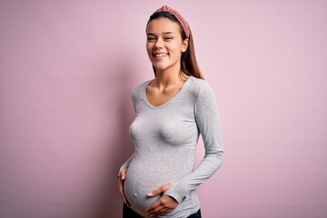 Young beautiful teenager girl pregnant expecting baby over isolated pink background with a happy...