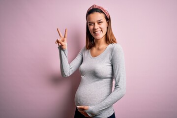 Young beautiful teenager girl pregnant expecting baby over isolated pink background smiling with...
