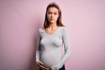 Young beautiful teenager girl pregnant expecting baby over isolated pink background skeptic and...