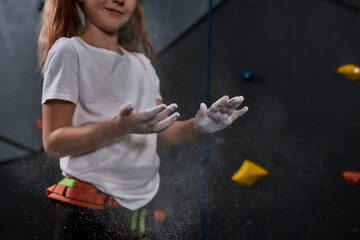 Cropped shot of sportive kid, girl applying white dust of magnesia, chalk on hands before climbing...