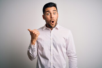 Young handsome man wearing elegant shirt standing over isolated white background Surprised pointing...