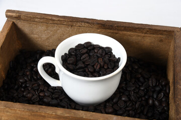 cup with roasted coffee beans inside, on the table with roasted beans top view,.