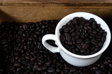cup with roasted coffee beans inside, on the table with roasted beans top view