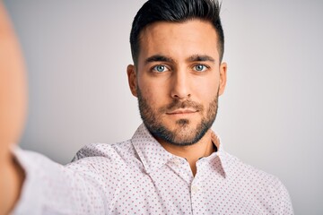 Fototapeta premium Young handsome man wearing shirt making selfie by the camera over white background with a confident expression on smart face thinking serious