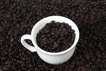 cup with roasted coffee beans inside, on the table with roasted beans top view,.
