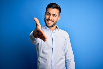 Young handsome man wearing elegant shirt standing over isolated blue background smiling friendly...