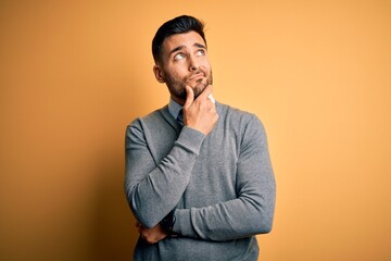 Young handsome businessman wearing elegant sweater and tie over yellow background with hand on chin thinking about question, pensive expression. Smiling with thoughtful face. Doubt concept.