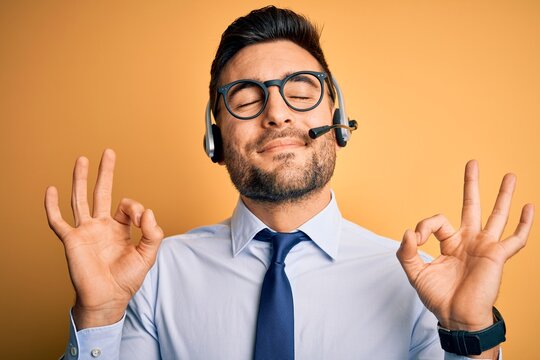 Young business operator man wearing customer service headset from call center relax and smiling with eyes closed doing meditation gesture with fingers. Yoga concept.