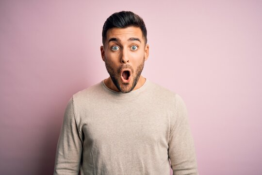 Young handsome man wearing casual sweater standing over isolated pink background afraid and shocked with surprise expression, fear and excited face.