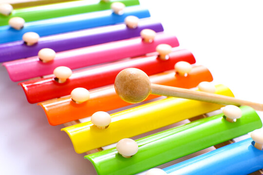 Rainbow colored wooden toy xylophone with wooden stick on white background, close up