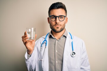 Young doctor man wearing stethoscope drinking a fresh glass of water over isolated background with a confident expression on smart face thinking serious