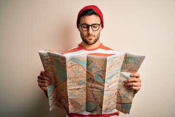 Fototapeta premium Young handsome tourist man on vacation wearing glasses holding city map with a confident expression on smart face thinking serious