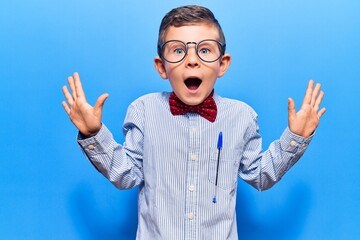 Fototapeta premium Cute blond kid wearing nerd bow tie and glasses celebrating crazy and amazed for success with arms raised and open eyes screaming excited. winner concept