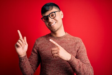 Young handsome hispanic man wearing nerd glasses over red background smiling and looking at the...