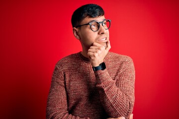 Obraz premium Young handsome hispanic man wearing nerd glasses over red background Thinking worried about a question, concerned and nervous with hand on chin