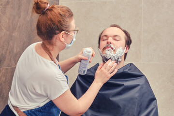 Woman applies shaving foam to a man in a home bathroom