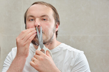 Face of a male adult close-up, who cuts his beard with scissors, copy space