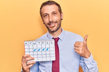 Young handsome man holding travel calendar smiling happy and positive, thumb up doing excellent and approval sign