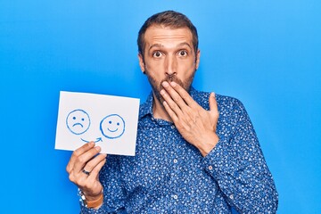 Young handsome man holding sad to happy emotion paper covering mouth with hand, shocked and afraid...