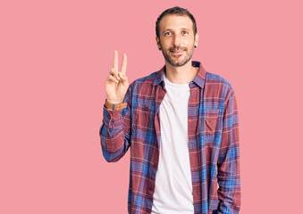 Young handsome man wearing casual clothes smiling looking to the camera showing fingers doing victory sign. number two.