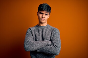 Young handsome man wearing casual sweater standing over isolated orange background skeptic and...