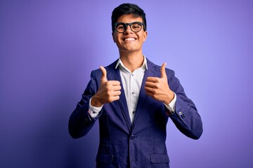 Young handsome business man wearing jacket and glasses over isolated purple background success sign doing positive gesture with hand, thumbs up smiling and happy. Cheerful expression and winner