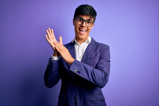 Young handsome business man wearing jacket and glasses over isolated purple background clapping and applauding happy and joyful, smiling proud hands together