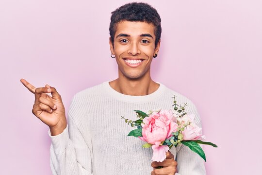 Young african amercian man holding flowers smiling happy pointing with hand and finger to the side