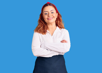 Young latin woman wearing waitress apron happy face smiling with crossed arms looking at the...