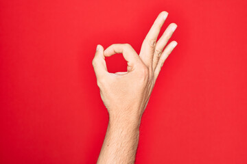 Hand of caucasian young man showing fingers over isolated red background gesturing approval...