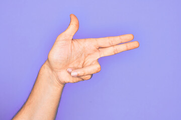 Hand of caucasian young man showing fingers over isolated purple background gesturing fire gun weapon with fingers, aiming shoot symbol