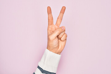 Hand of caucasian young man showing fingers over isolated pink background counting number 2 showing two fingers, gesturing victory and winner symbol