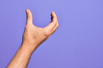 Hand of caucasian young man showing fingers over isolated purple background picking and taking invisible thing, holding object with fingers showing space