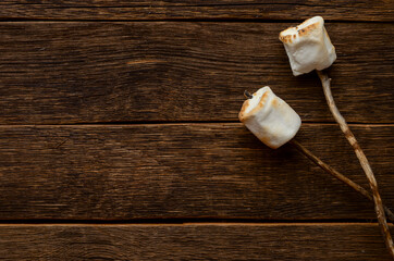 Marshmallow on the stick on wooden background
