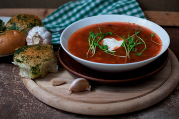 Red borsch with garlic pampusks, peas sprouts and garlic on dark brown background. Traditional dish of ukrainian cuisine. 
