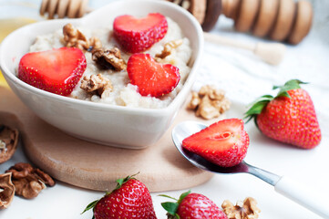 Breakfast with oatmeal with strawberries, honey, walnuts and egg on white background. Breakfast for child. Oatmeal in a white heart-shaped bowl
