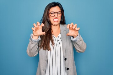 Young hispanic business woman wearing glasses standing over blue isolated background smiling funny doing claw gesture as cat, aggressive and sexy expression