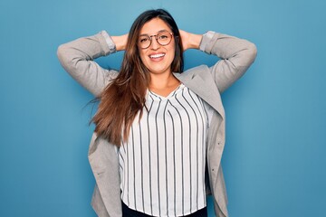 Young hispanic business woman wearing glasses standing over blue isolated background relaxing and...