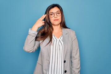 Young hispanic business woman wearing glasses standing over blue isolated background Shooting and killing oneself pointing hand and fingers to head like gun, suicide gesture.