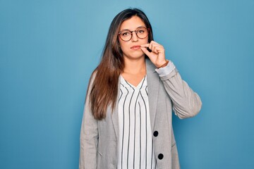 Young hispanic business woman wearing glasses standing over blue isolated background mouth and lips...